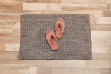 Photo of New grey bath mat with fluffy slippers on floor, top view