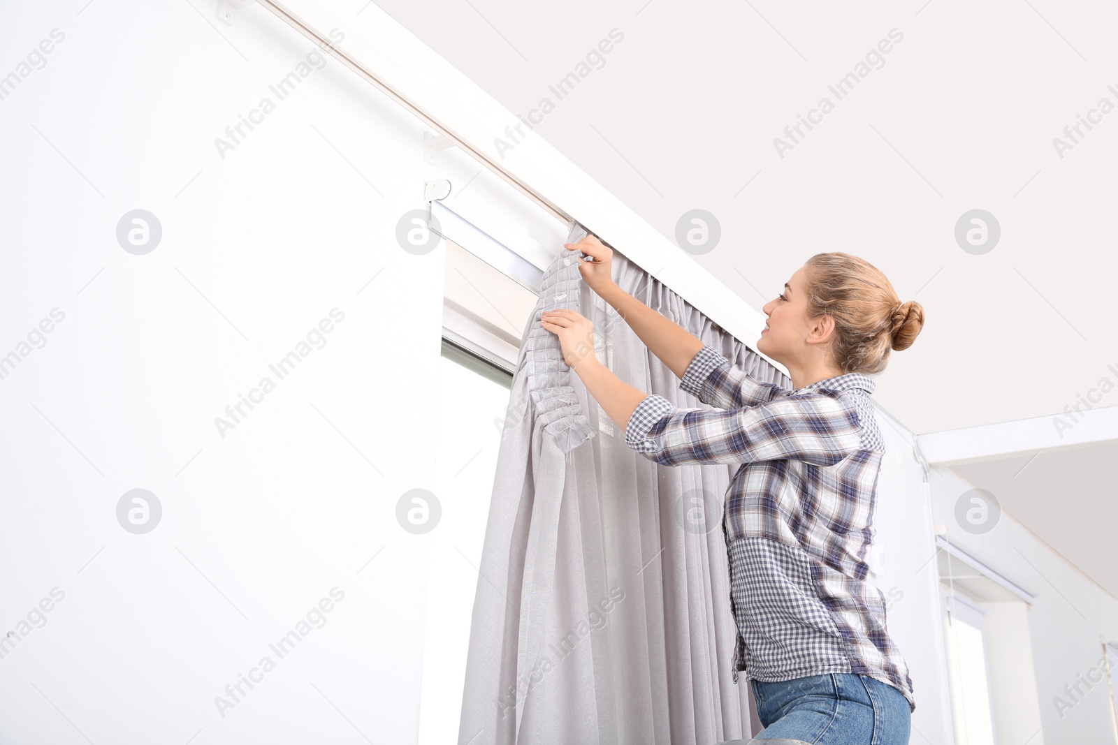 Photo of Woman hanging window curtain indoors. Interior decor element