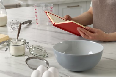 Photo of Woman with recipe book at white marble table in kitchen, closeup