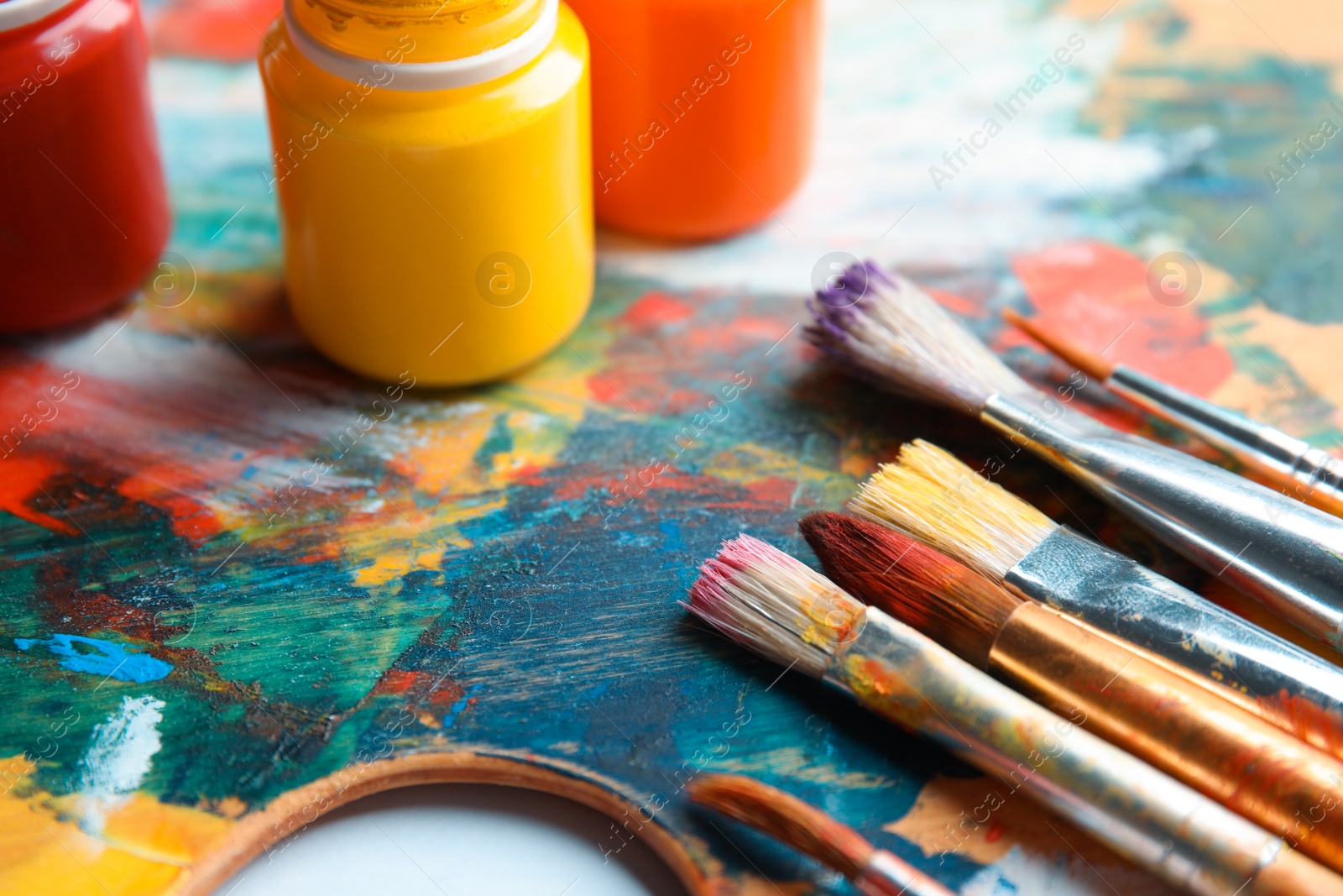 Photo of Different brushes and jars with paint on palette, closeup
