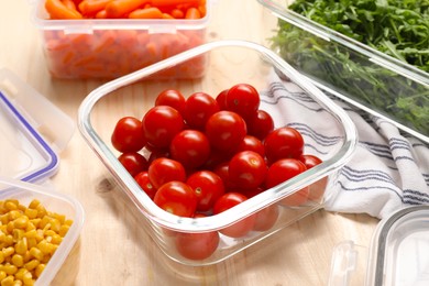 Photo of Containers with tomatoes and fresh products on wooden table, closeup. Food storage