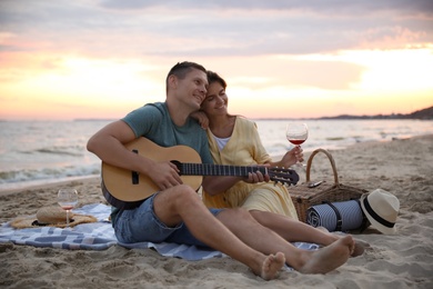 Photo of Lovely couple with guitar and picnic basket on beach at sunset