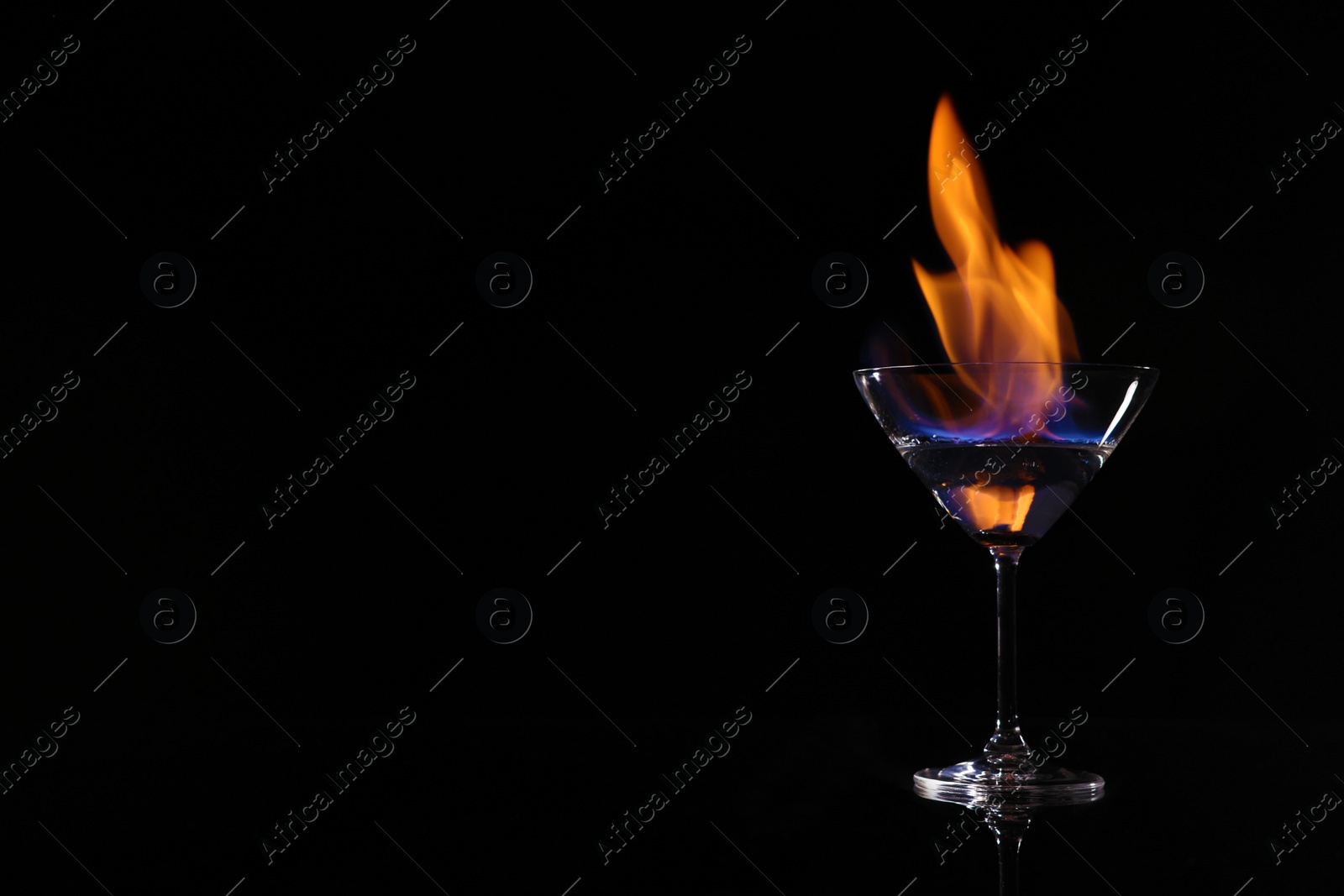 Photo of Cocktail glass with flaming vodka on black background, space for text