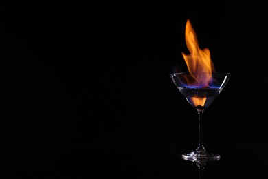 Photo of Cocktail glass with flaming vodka on black background, space for text