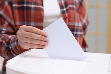 Photo of Woman putting her vote into ballot box on blurred background, closeup