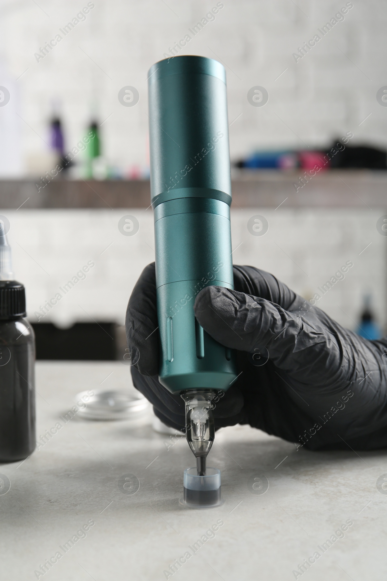 Photo of Tattoo artist with professional machine and ink at white table in salon, closeup