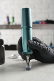 Tattoo artist with professional machine and ink at white table in salon, closeup