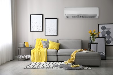 Image of Modern air conditioner on light grey wall in living room with stylish sofa