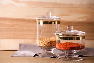 Photo of Jars with cereals on table against wooden background, space for text. Foodstuff for modern kitchen