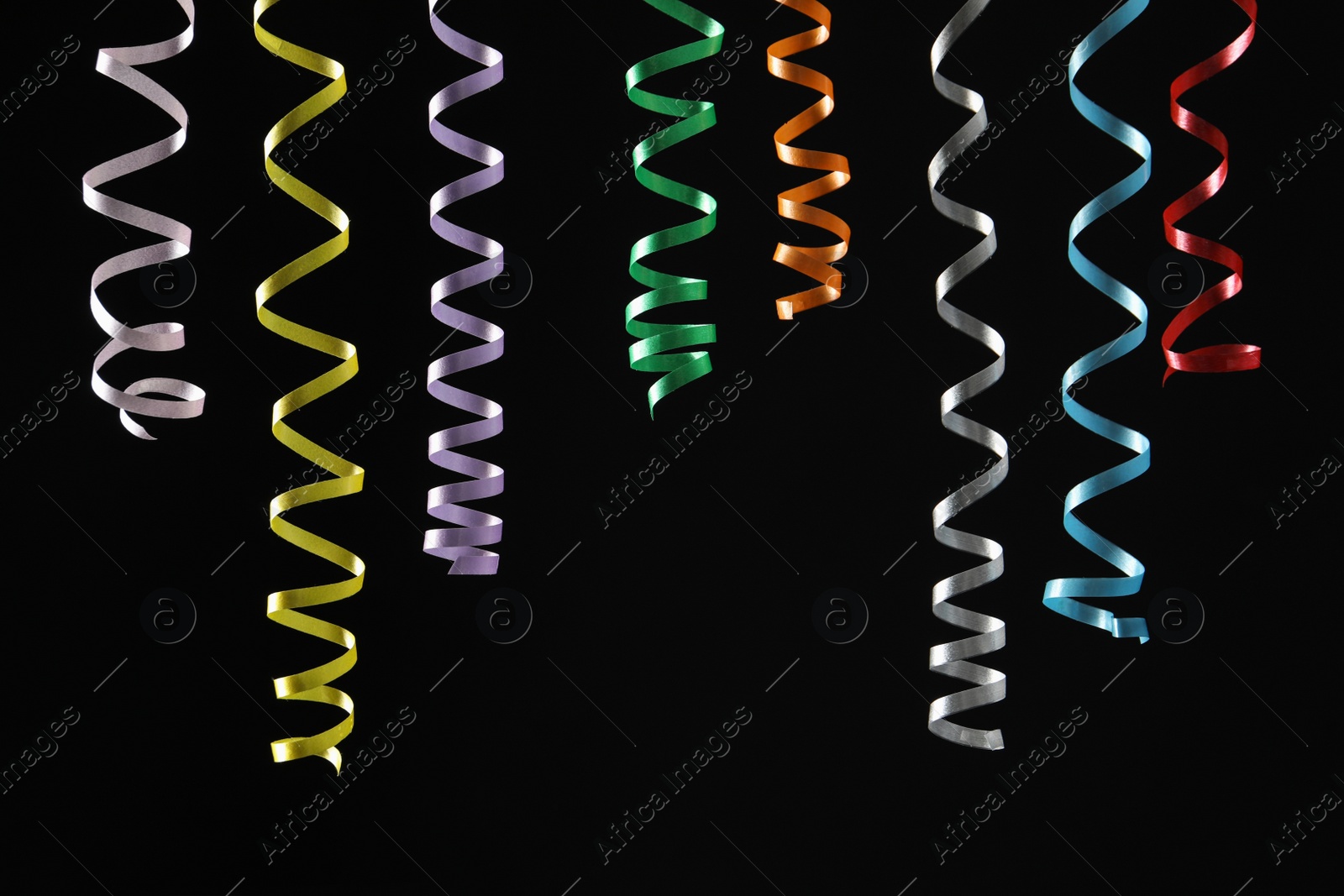 Photo of Many colorful serpentine streamers on black background