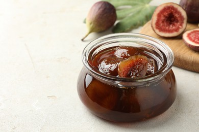 Jar of tasty sweet jam and fresh figs on white table, space for text