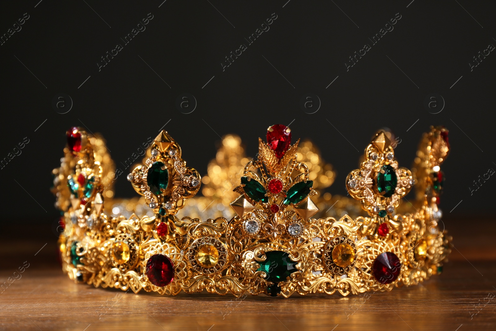 Photo of Beautiful golden crown with gems on wooden table. Fantasy item