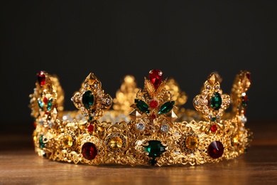 Photo of Beautiful golden crown with gems on wooden table. Fantasy item