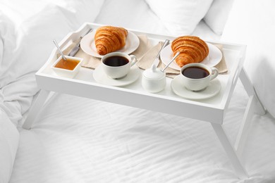 Photo of Tasty breakfast served in bed. Fresh croissants, coffee and honey on tray