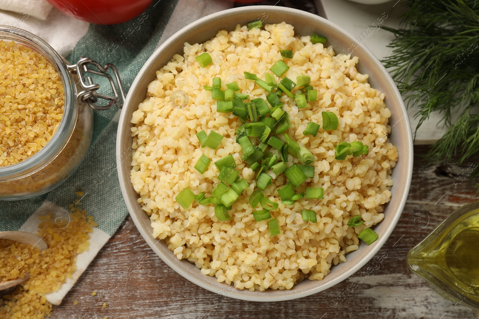 Photo of Delicious bulgur with green onion in bowl on wooden table, top view