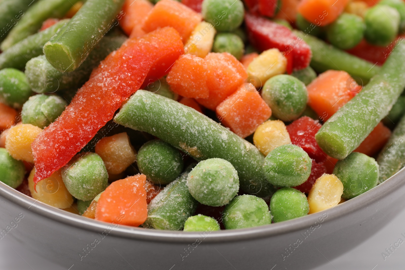 Photo of Mix of different frozen vegetables in bowl on white table, closeup