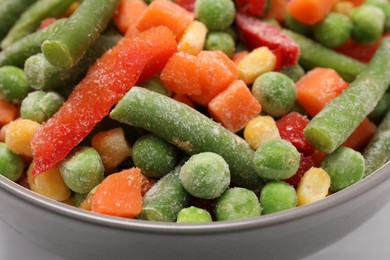 Mix of different frozen vegetables in bowl on white table, closeup