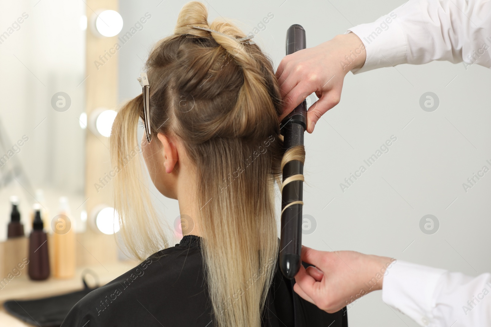 Photo of Hair styling. Hairdresser curling woman's hair in salon, closeup