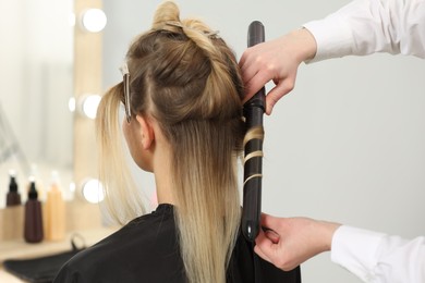 Photo of Hair styling. Hairdresser curling woman's hair in salon, closeup