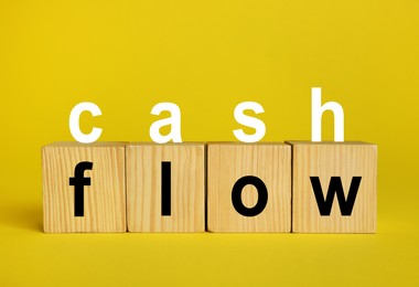Image of Phrase Cash Flow made with letters and wooden cubes on yellow background