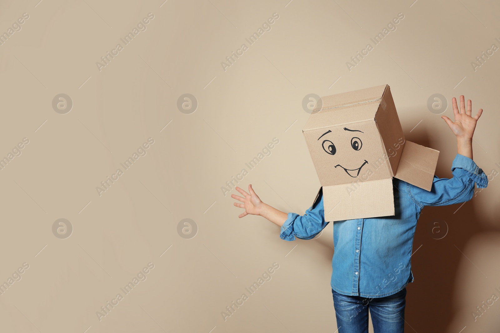 Photo of Cute little child wearing cardboard box with smiling face on color background. Space for text