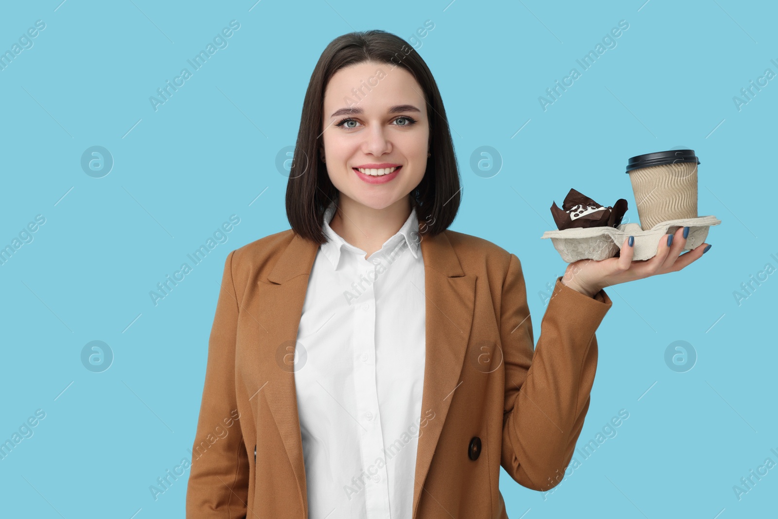 Photo of Happy young intern holding takeaway cup and muffin on light blue background