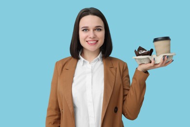 Photo of Happy young intern holding takeaway cup and muffin on light blue background