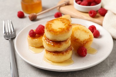 Delicious cottage cheese pancakes with raspberries and honey on light grey table, closeup