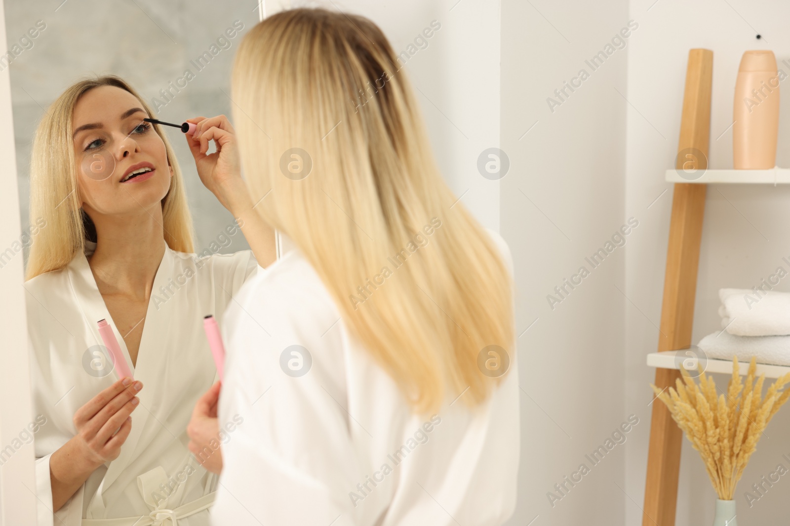 Photo of Beautiful woman applying mascara near mirror in bathroom