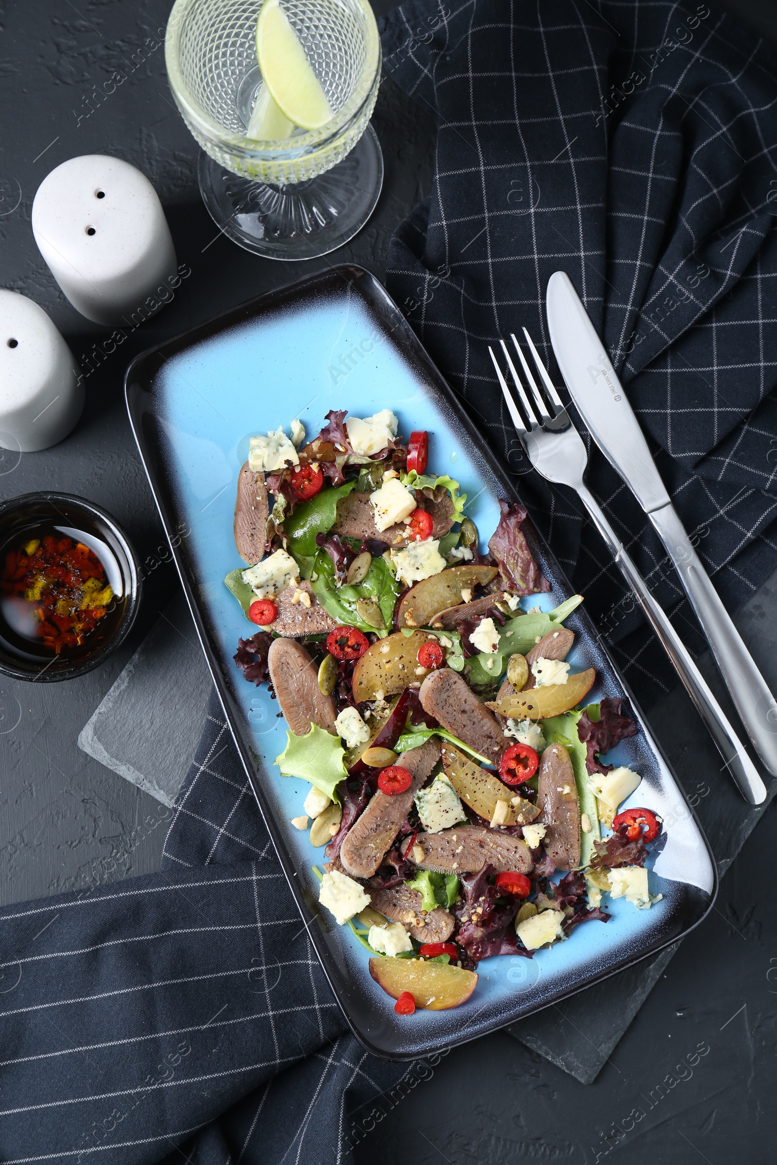 Photo of Delicious salad with beef tongue and cheese served on black textured table, flat lay