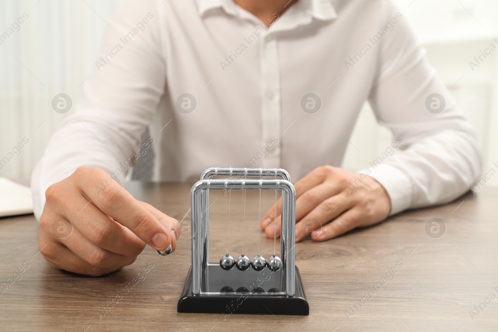 Photo of Man playing with Newton's cradle at wooden table, closeup. Physics law of energy conservation