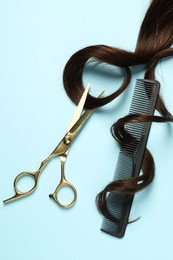 Professional hairdresser scissors and comb with brown hair strand on light blue background, flat lay