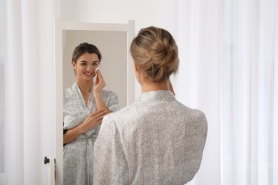 Photo of Beautiful young woman cleaning her face near mirror in room