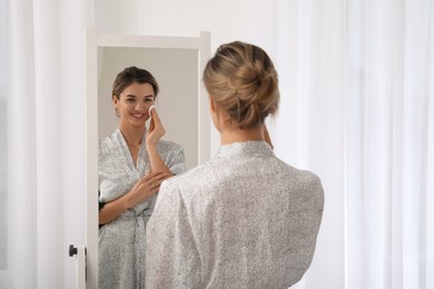 Beautiful young woman cleaning her face near mirror in room