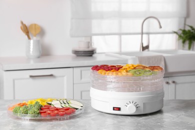 Photo of Cut fruits, vegetables and dehydrator machine on grey marble table in kitchen