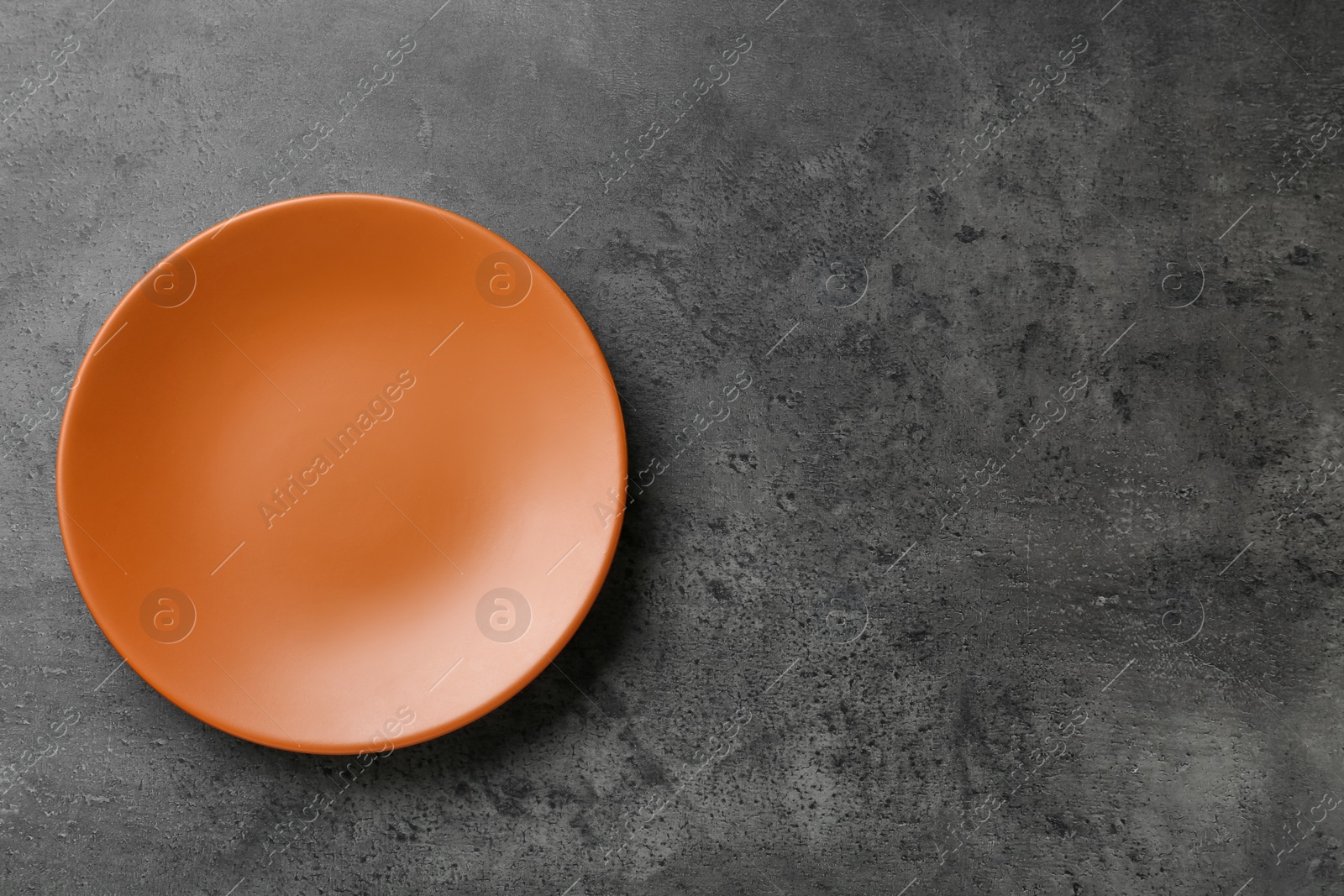 Photo of Clean orange plate on grey table, top view. Space for text