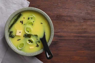 Photo of Bowl of delicious miso soup with tofu and spoon on wooden table, top view. Space for text