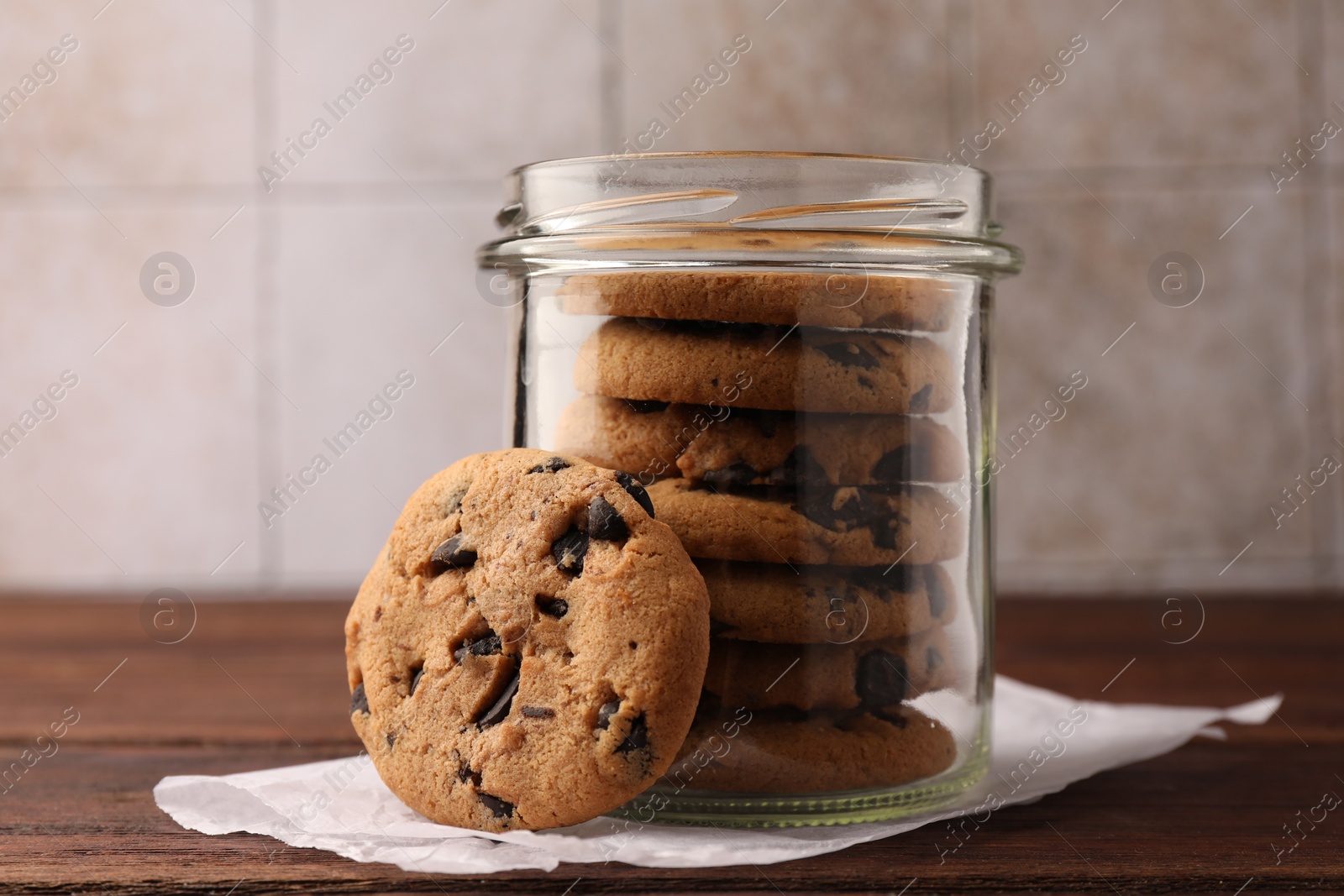 Photo of Glass jar with delicious chocolate chip cookies on wooden table