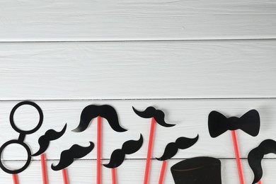 Fake paper mustaches, bow tie and monocle party props on white wooden background, flat lay. Space for text