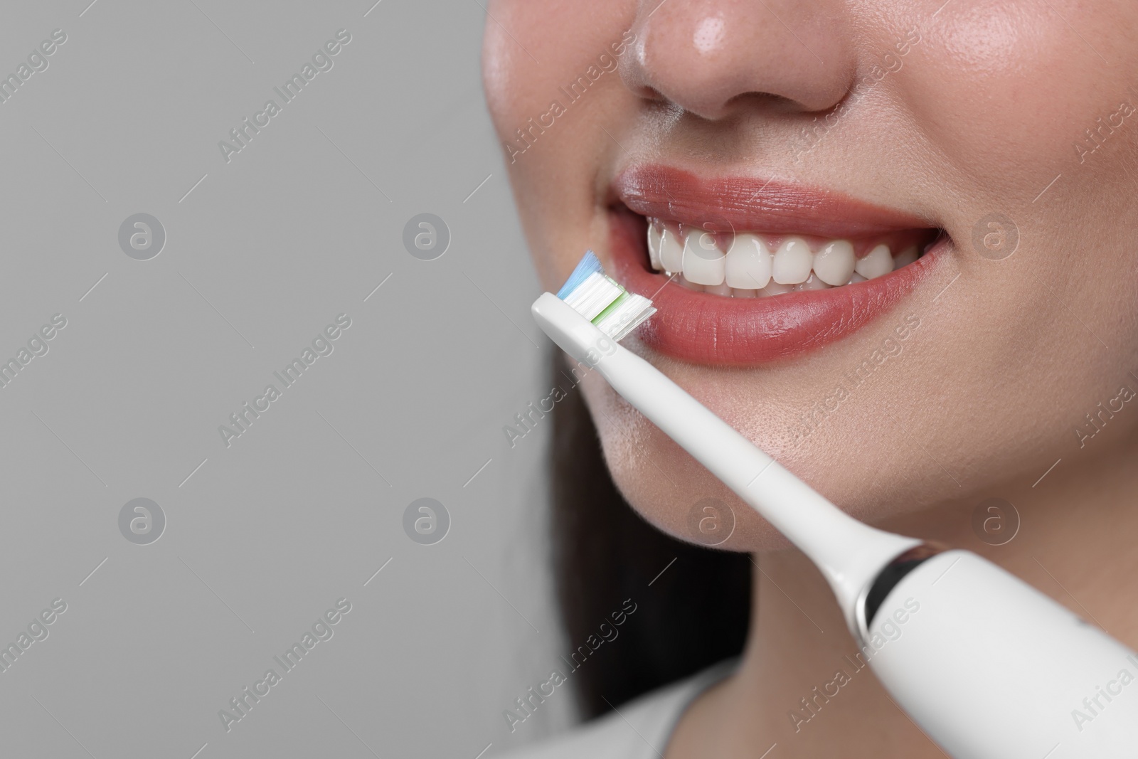 Photo of Woman brushing her teeth with electric toothbrush on light grey background, closeup. Space for text