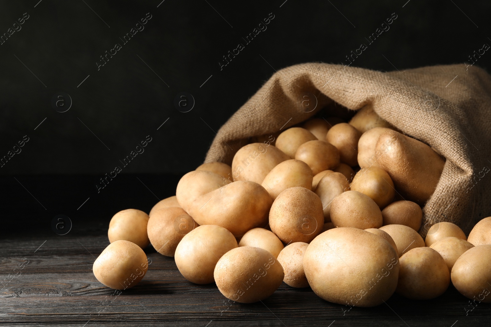 Photo of Raw fresh organic potatoes on wooden table against dark background. Space for text