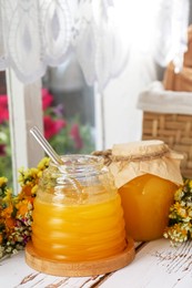 Photo of Delicious fresh honey and beautiful flowers on white wooden table indoors