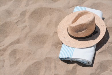 Photo of Straw hat and beach towel on sand, space for text
