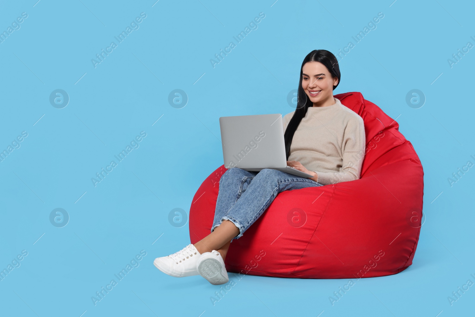 Photo of Happy woman with laptop sitting on beanbag chair against light blue background