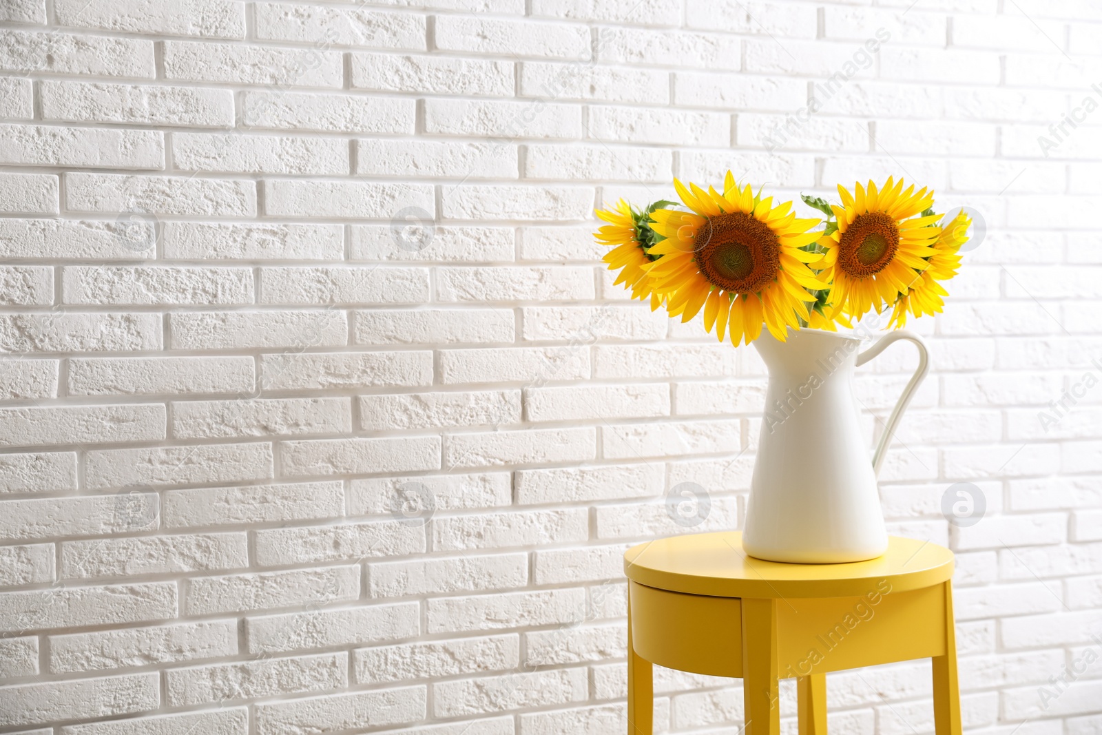 Photo of Bouquet of beautiful sunflowers on table near white brick wall. Space for text