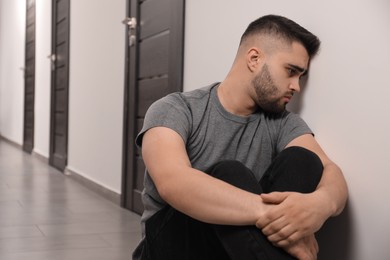 Photo of Sad man sitting on floor in hall. Space for text