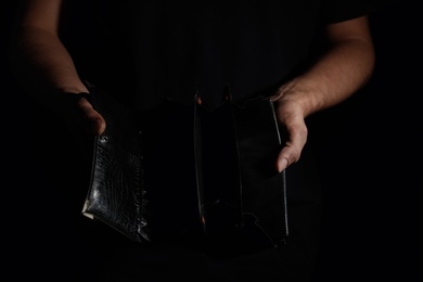 Photo of Poor man with empty wallet on dark background, closeup