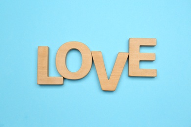 Word LOVE made of wooden letters on light blue background, flat lay