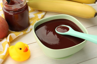 Bowl and spoon with tasty pureed baby food near ingredients on white wooden table