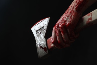 Photo of Man holding bloody axe on black background, closeup. Space for text